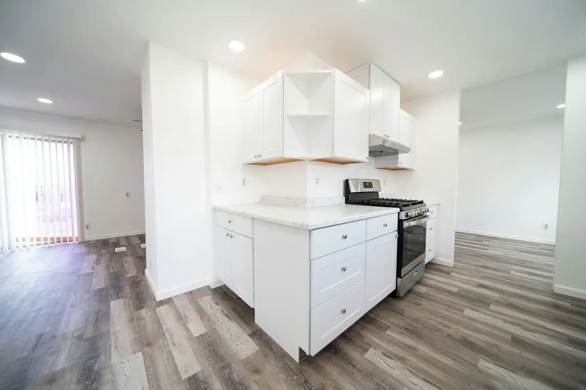 Empty open-plan kitchen with white cabinets, a stainless gas range and grey flooring extending into a bare living area