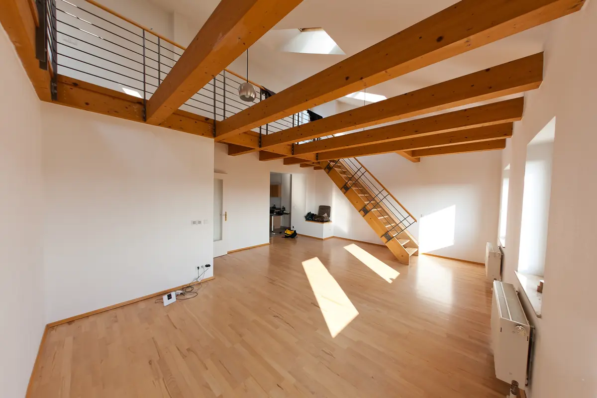 Empty loft with pale wood flooring, exposed timber beams, an open staircase and steel gallery railings