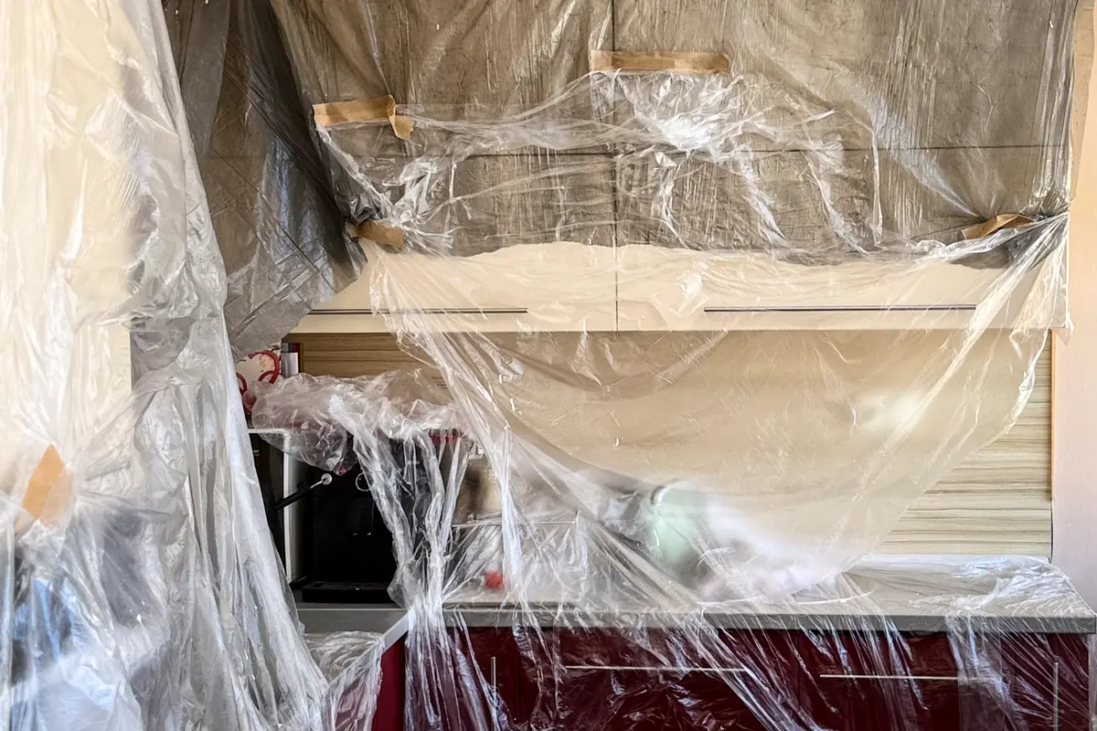 Kitchen cabinets and worktop sealed under clear plastic film taped with paper tape during renovation work