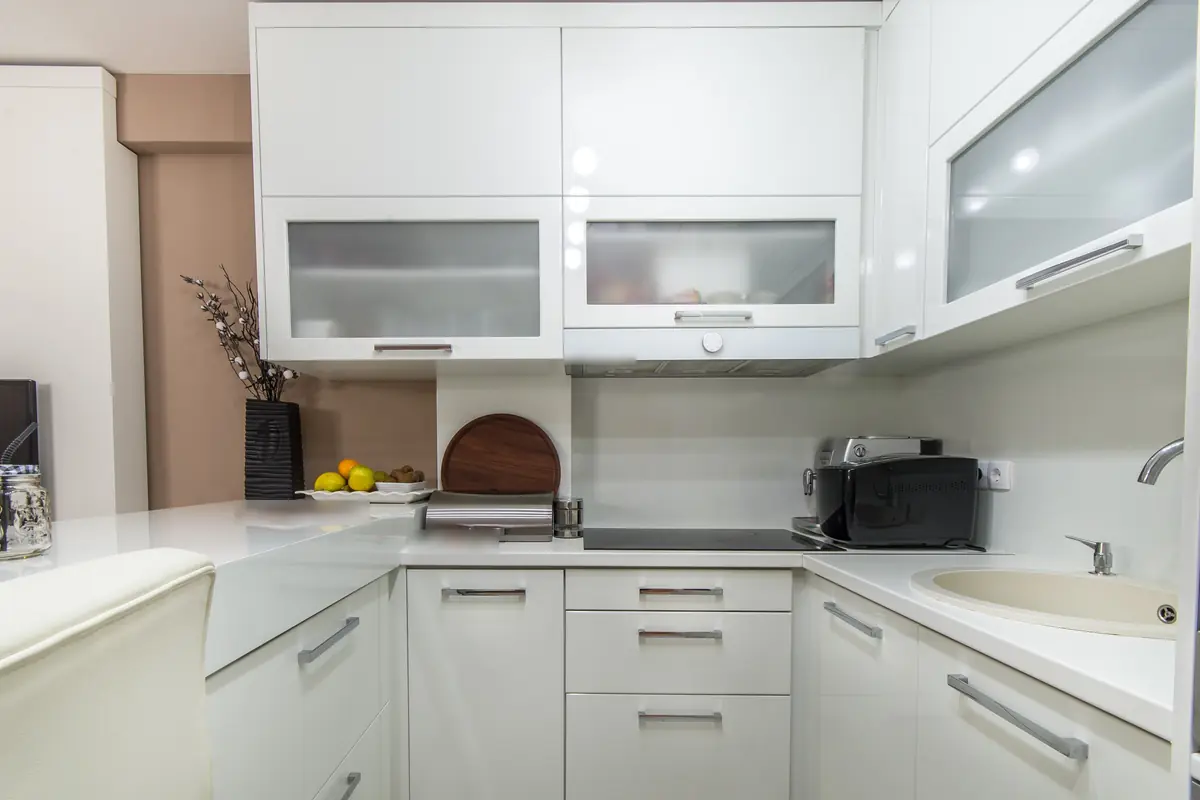 Compact kitchen with glossy white cupboards, frosted glass cabinet fronts, white counters and a round cream sink