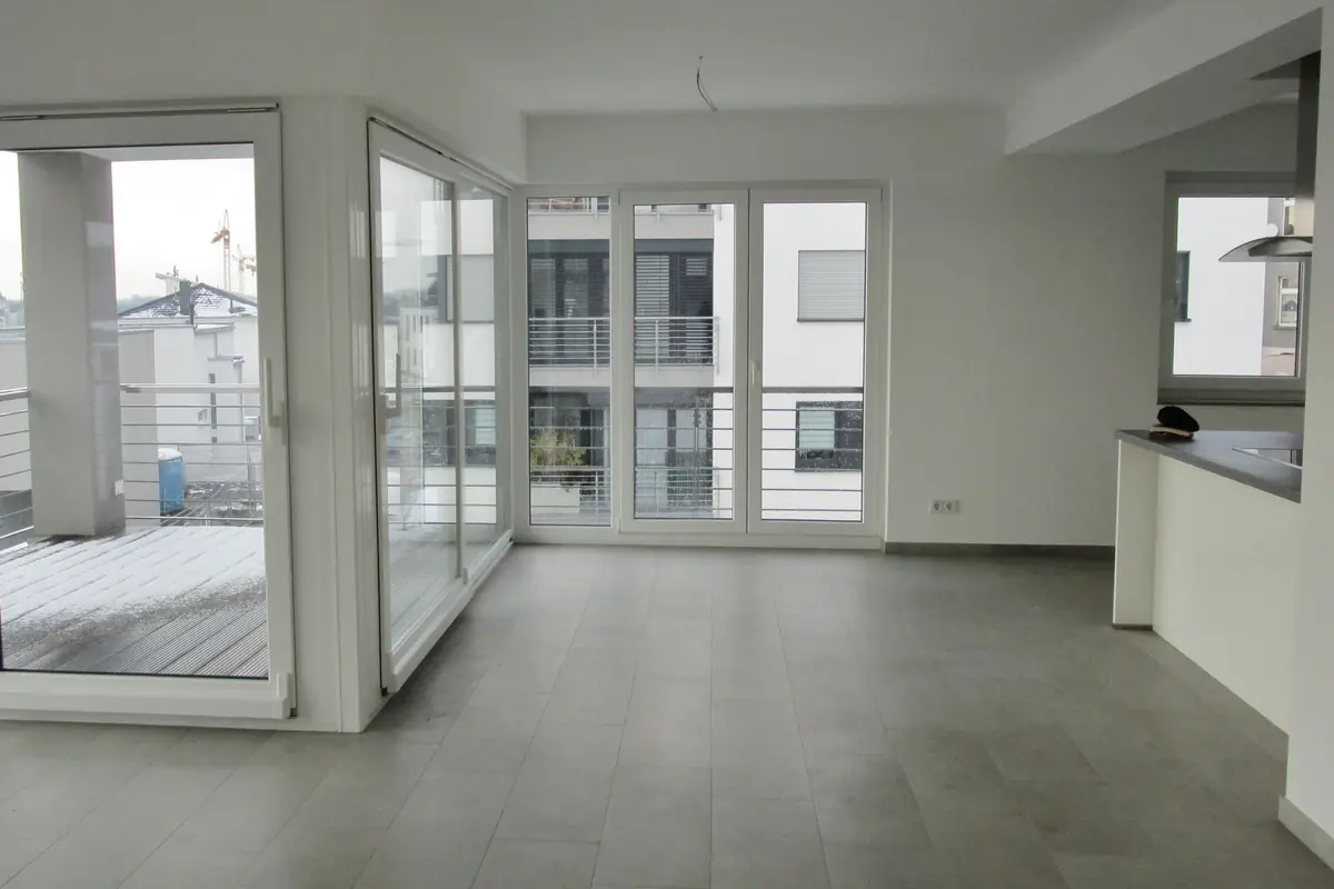 Vacant new flat with grey floor tiles, floor-to-ceiling window doors and construction cranes visible outside on the building site