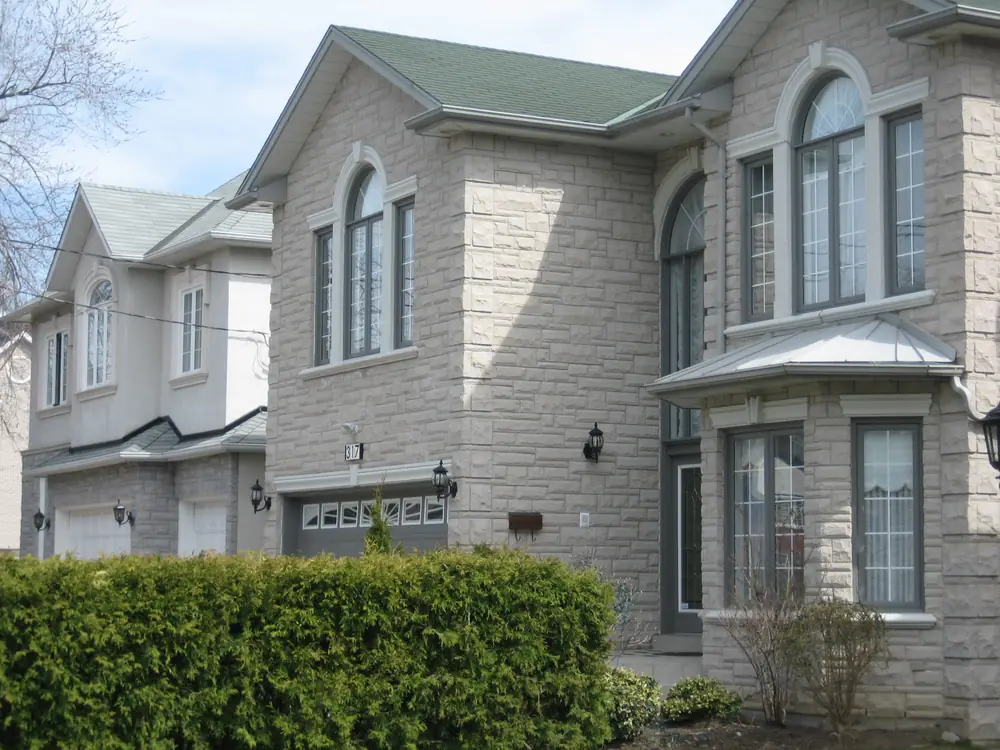 Two new stone-clad detached houses with garages behind a hedge in Willowdale, North York, Toronto
