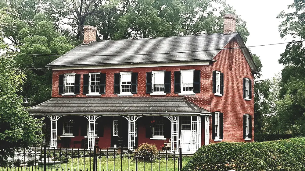 Brazel House, a red-brick farmhouse with a long veranda behind an iron fence in Bradford West Gwillimbury