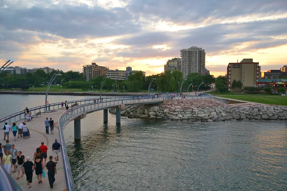 People walking on the Brant Street Pier above Lake Ontario, with Spencer Smith Park and downtown Burlington behind