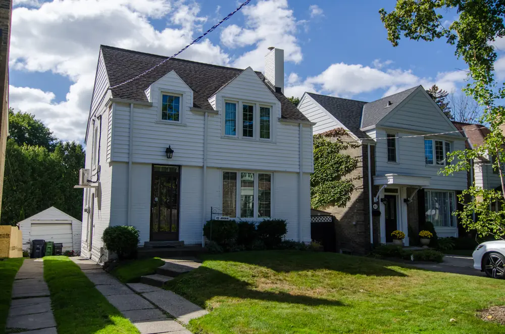 White detached houses with lawns and a front walk on Airdrie Road, Leaside, Toronto