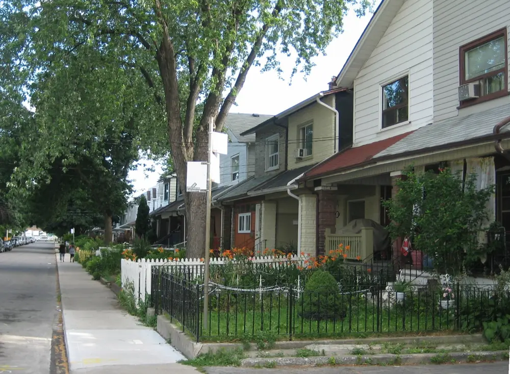 Narrow houses with front porches and small gardens behind iron fences in Leslieville, Toronto