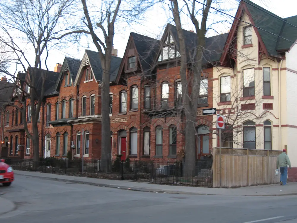 A row of red-brick Victorian houses with steep gables on a corner in Toronto