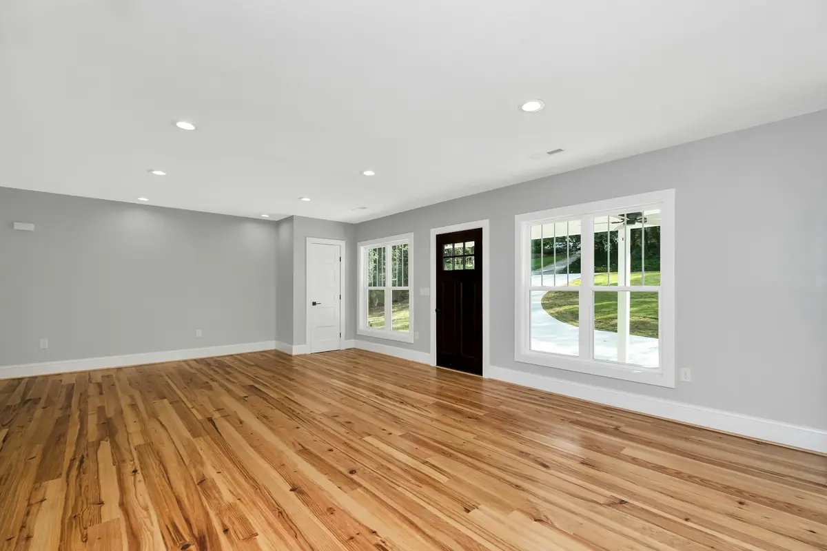 A freshly renovated, empty living room with new hardwood floors and pale grey walls