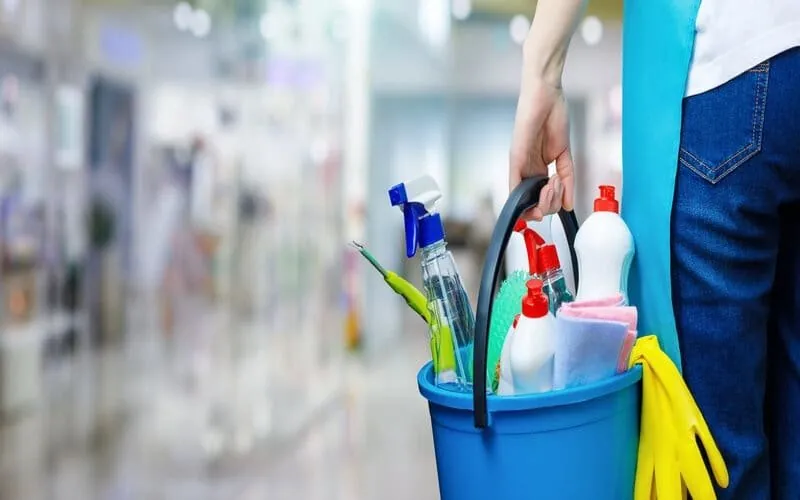 A cleaner carrying a bucket of cleaning supplies
