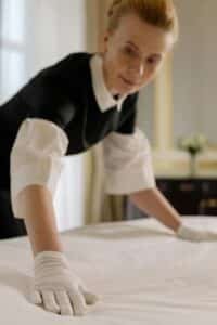 Maid organizing a bed with white gloves, professional cleaners 