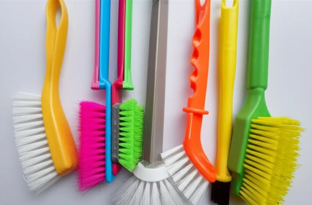 Row of colourful scrub brushes with plastic handles hanging on a wall