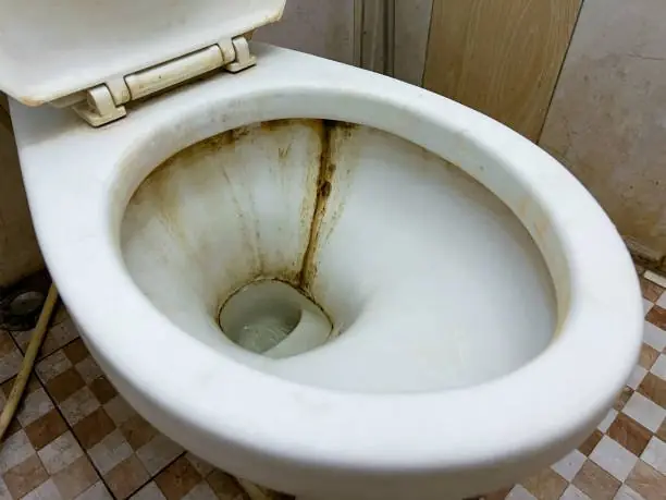 Close-up of a toilet bowl with brown stains and limescale streaks