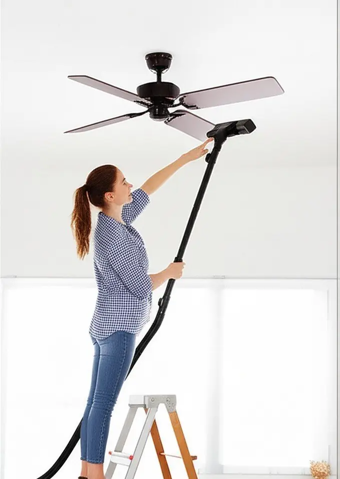 woman cleaning a ceiling fan with a vacuum cleaner